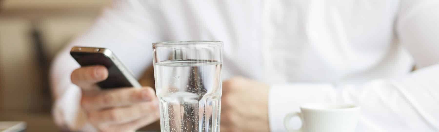 glass of water infron of a woman on her phone
