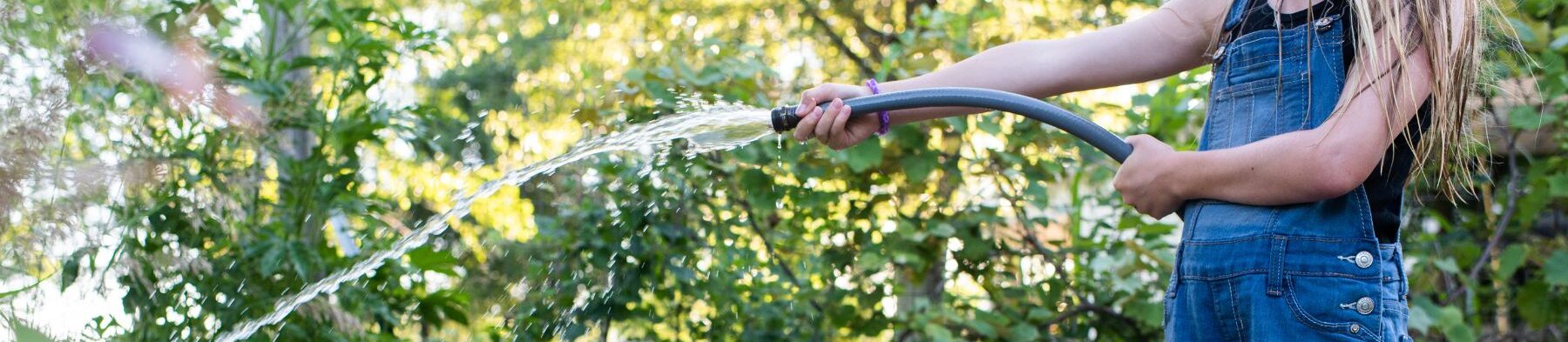 child using a watering hose to spray water