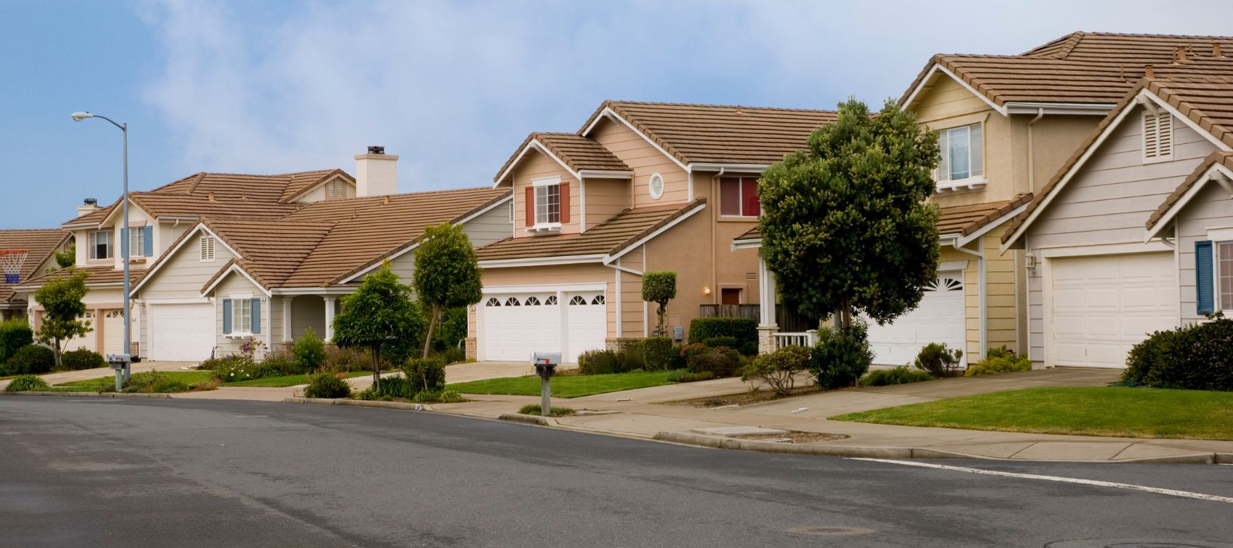 A row of suburban houses with well-kept lawns and driveways on a quiet residential street