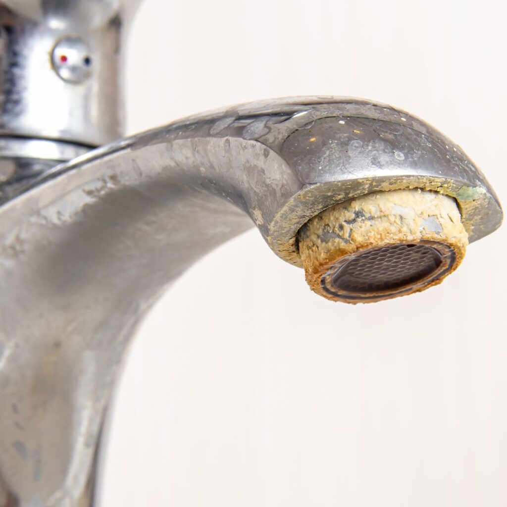 Close-up of a bathroom faucet heavily coated with crusty white and yellow hard water mineral deposits