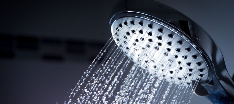 closeup of a shower head spraying water out of it in a dark setting